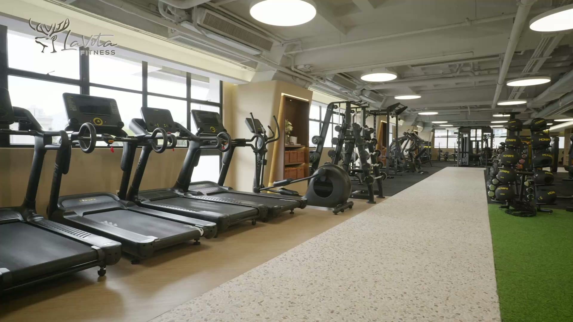 健身區全景:一排跑步機、大窗自然光與人造草地訓練區